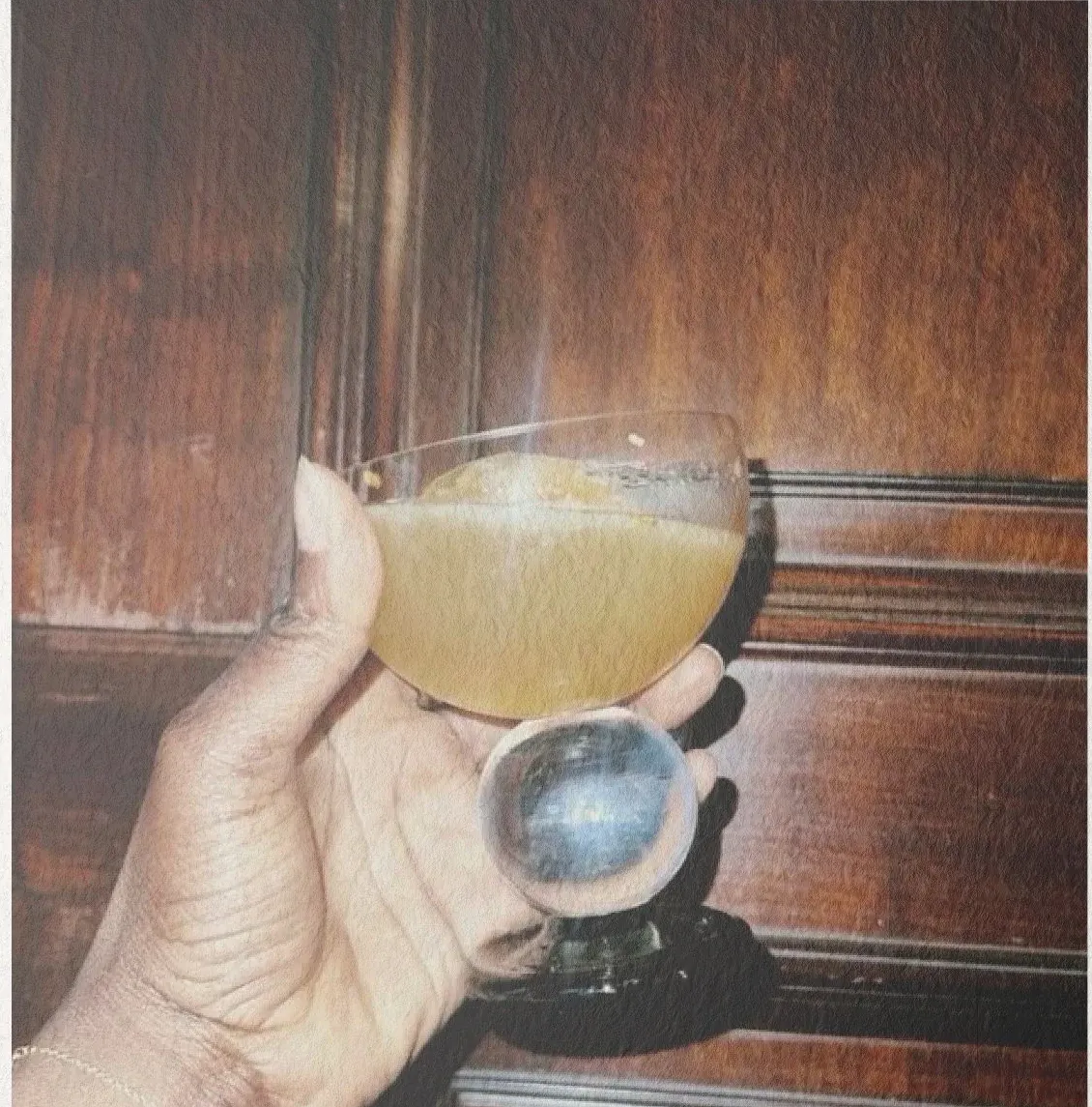 A hand holding a cocktail glass in warm, moody light at Ū Villas